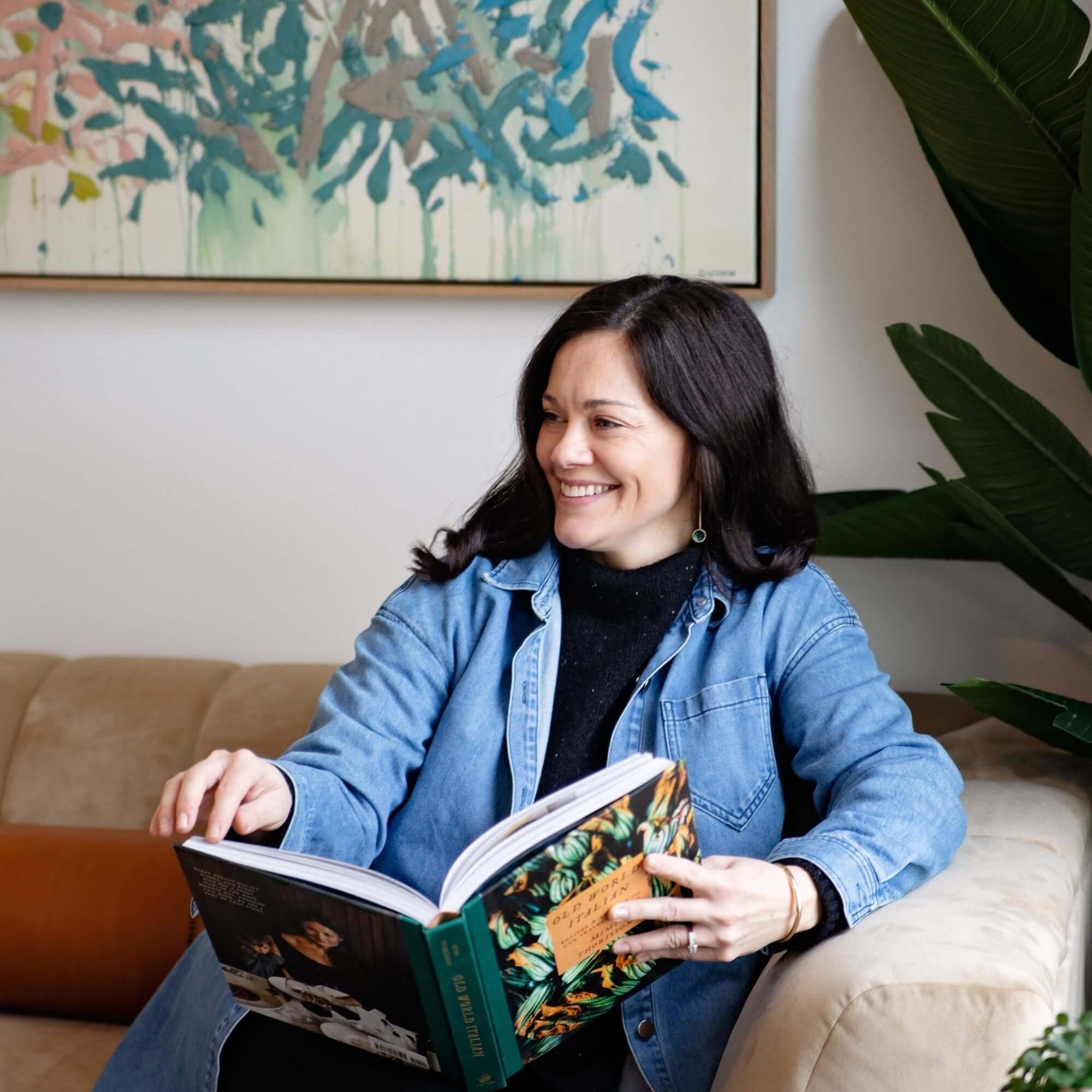 Alisha reading a book on a couch with a colorful abstract painting in the background