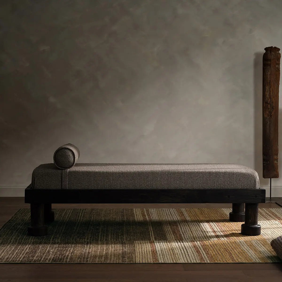 Long, narrow bench with a textured surface in a room with a textured wall and rug.