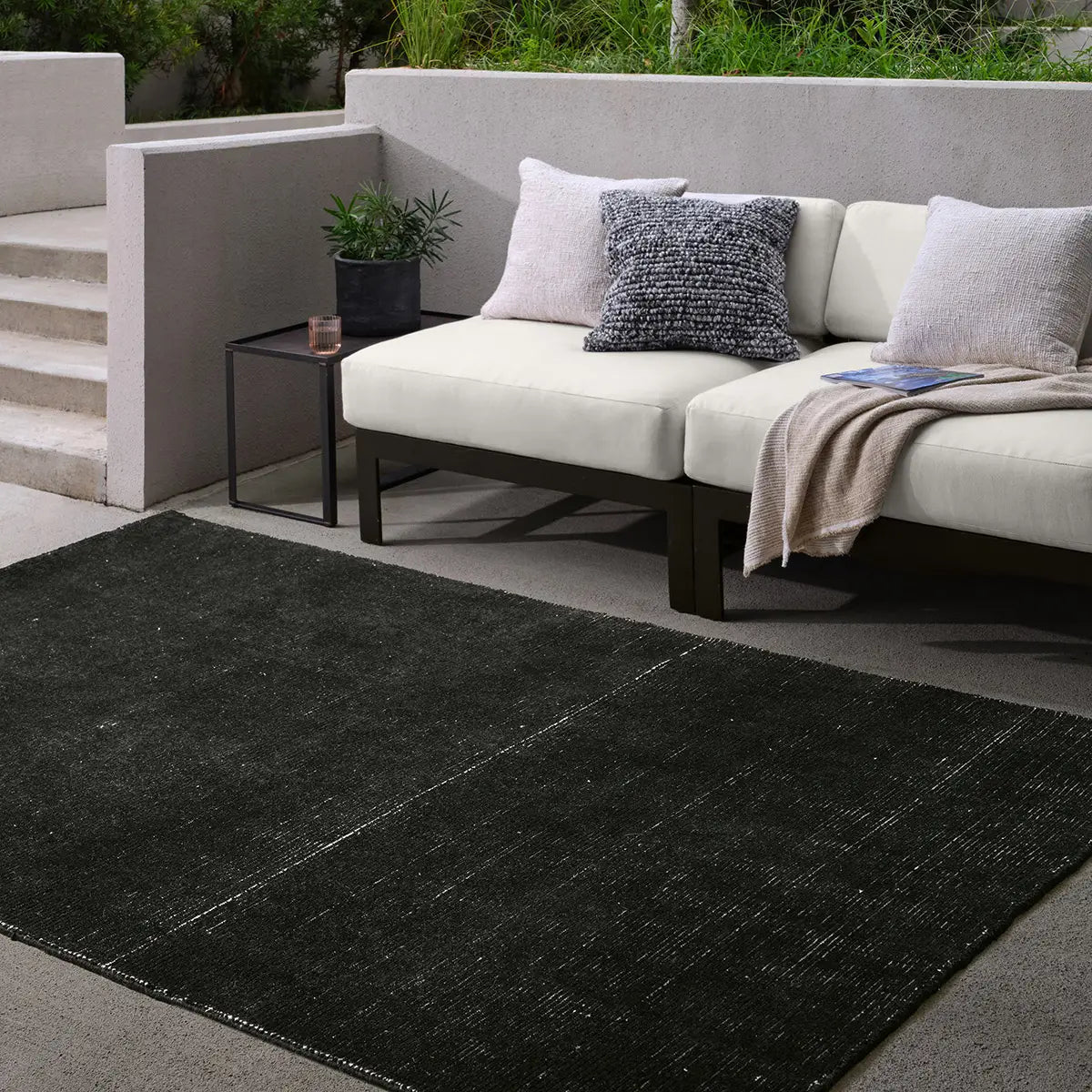 Outdoor seating area with a black rug, sofa, and small table.