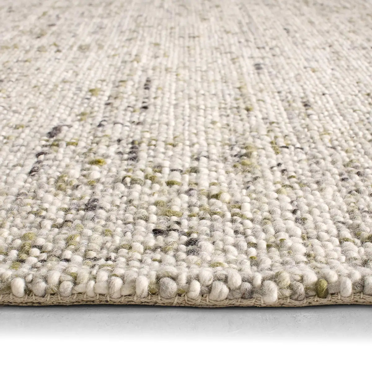 Close-up of a textured beige rug with specks of green and brown on a light gray background