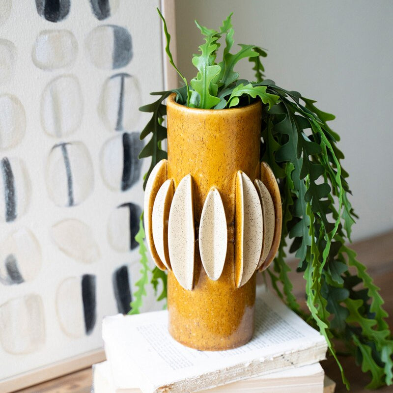 Decorative vase with plant on a stack of books against a textured wall.