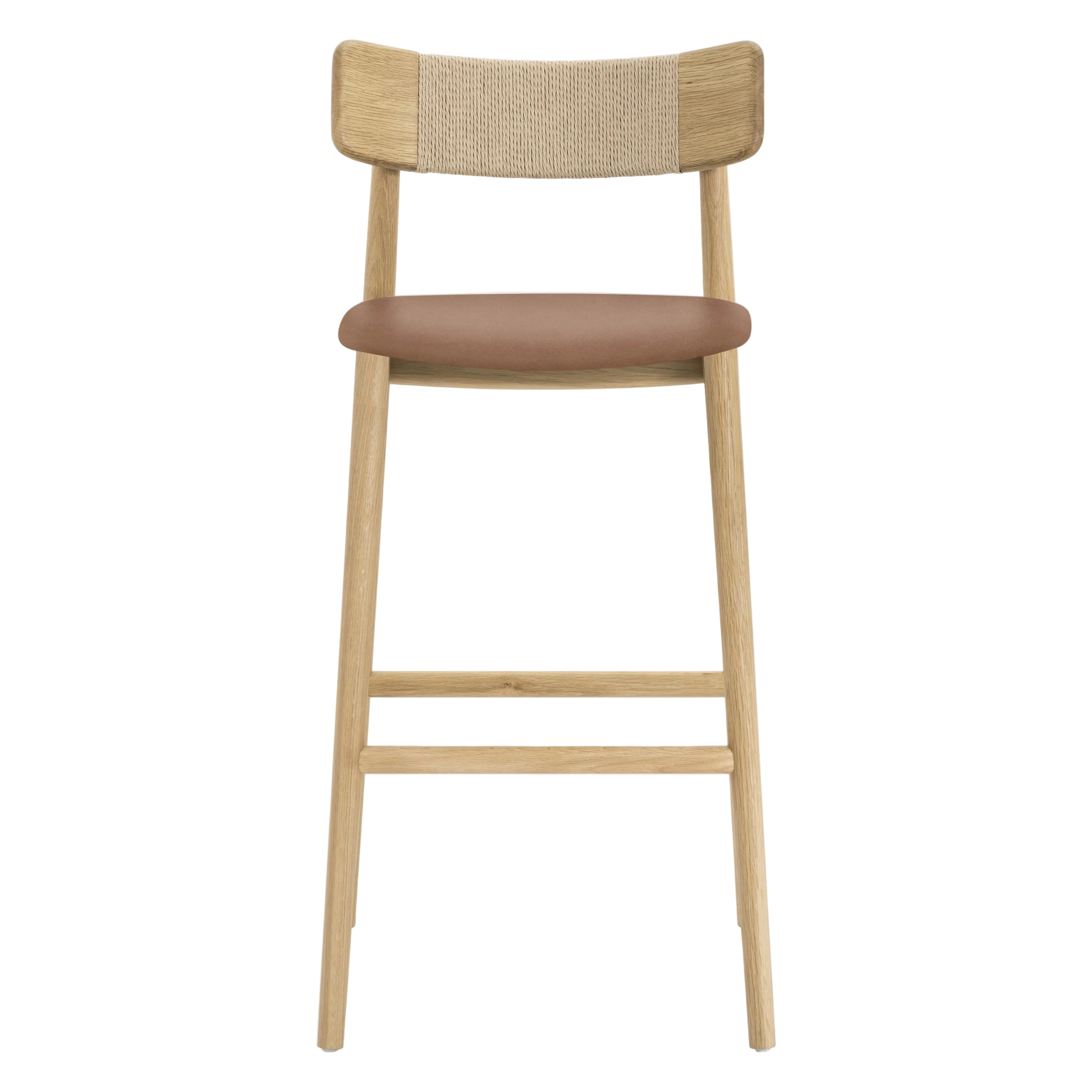 A modern wooden bar stool with a light natural oak frame, a woven cane backrest, and a brown upholstered seat cushion, shown against a plain white background.
