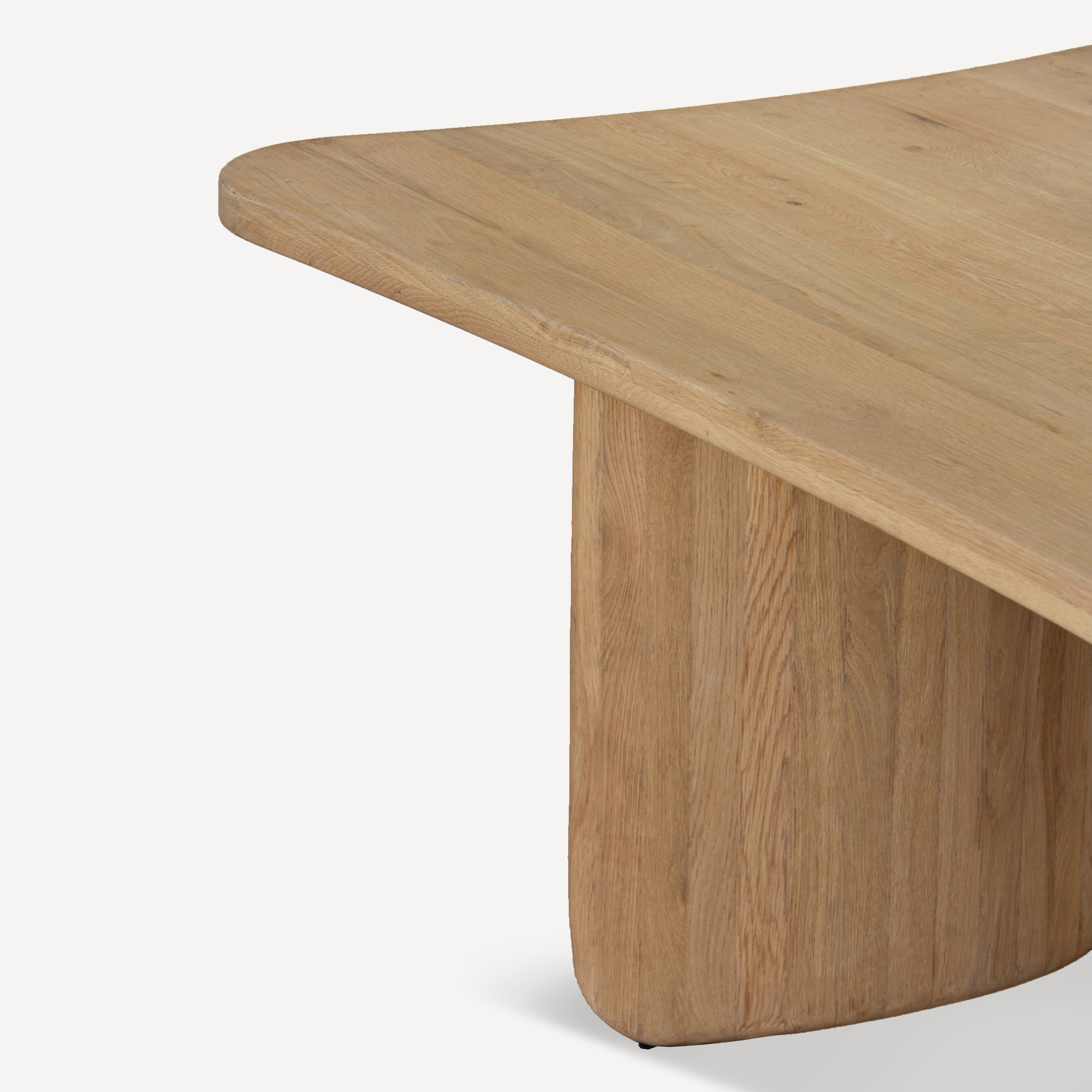 Close-up of a light oak wood dining table showing the rounded corner of the tabletop and the thick cylindrical pedestal base against a clean white background.