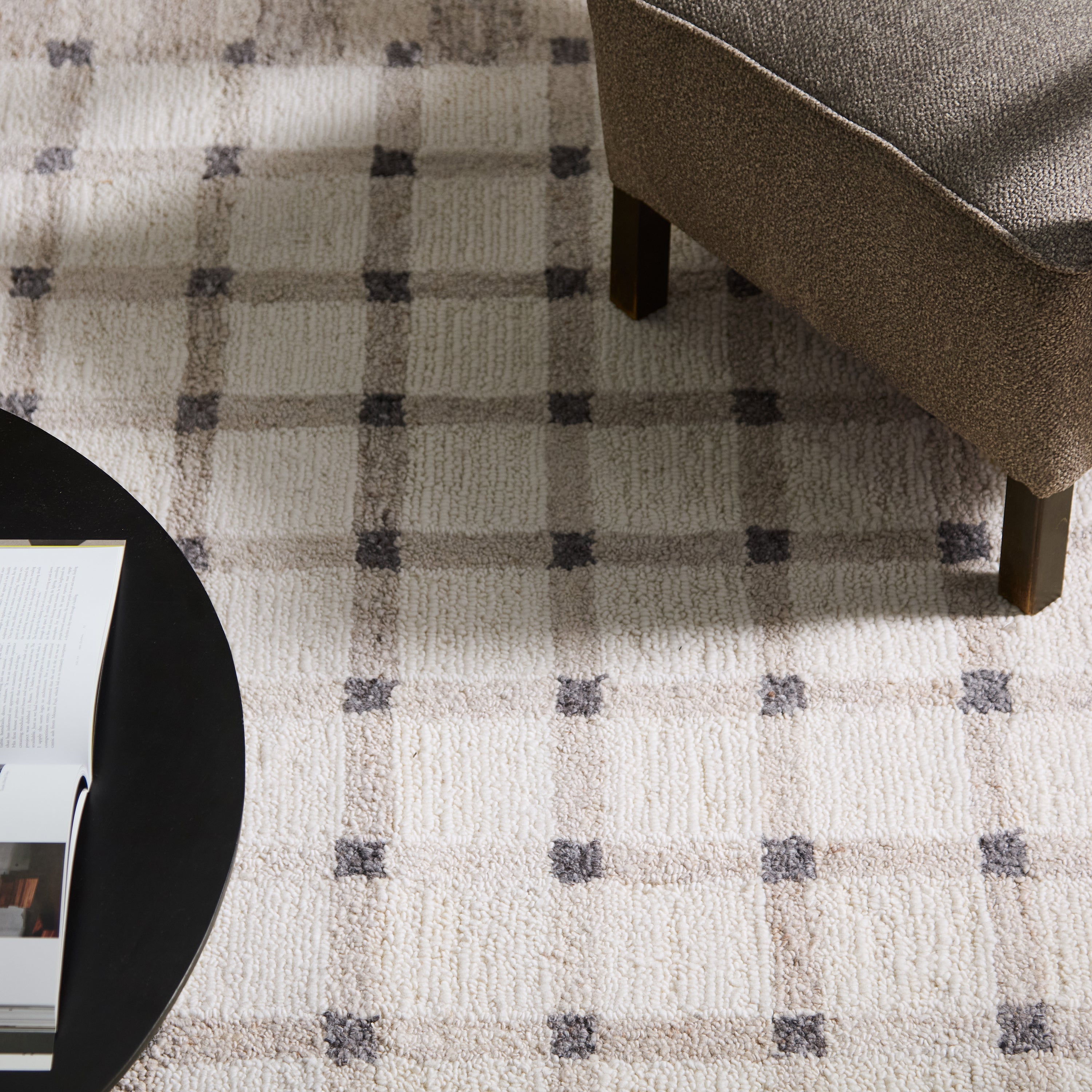 Plaid patterned rug with a corner of a chair and a round table visible.