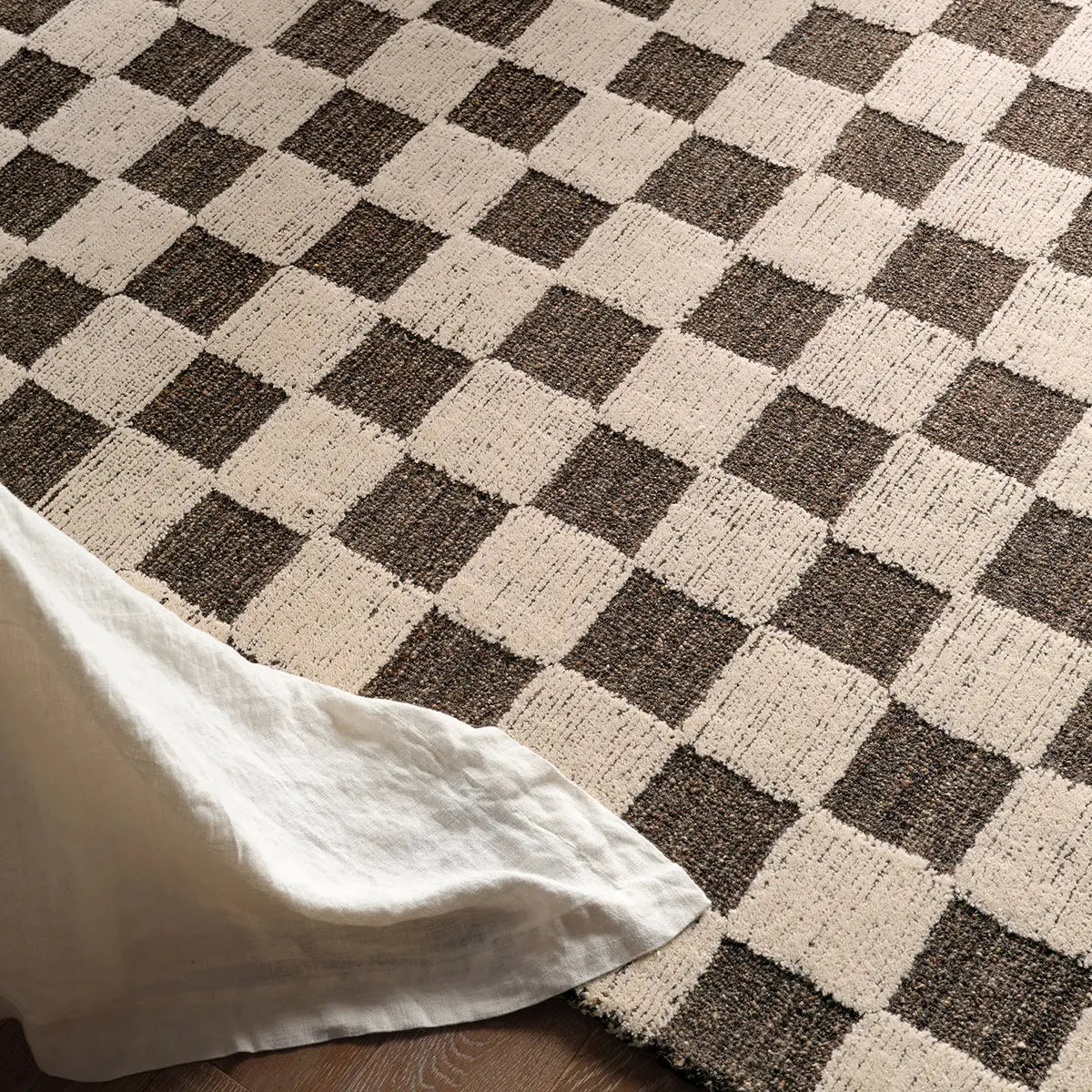 Checkered brown and beige rug with a white fabric corner.