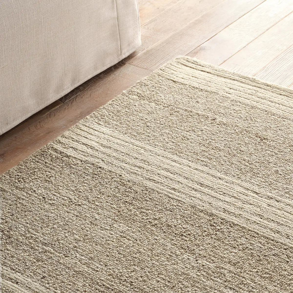 Textured beige rug on a wooden floor with a corner of a light-colored sofa.