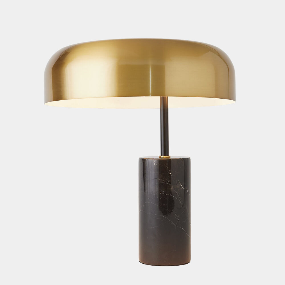 Table lamp with brass shade and dark cylindrical base on a white background