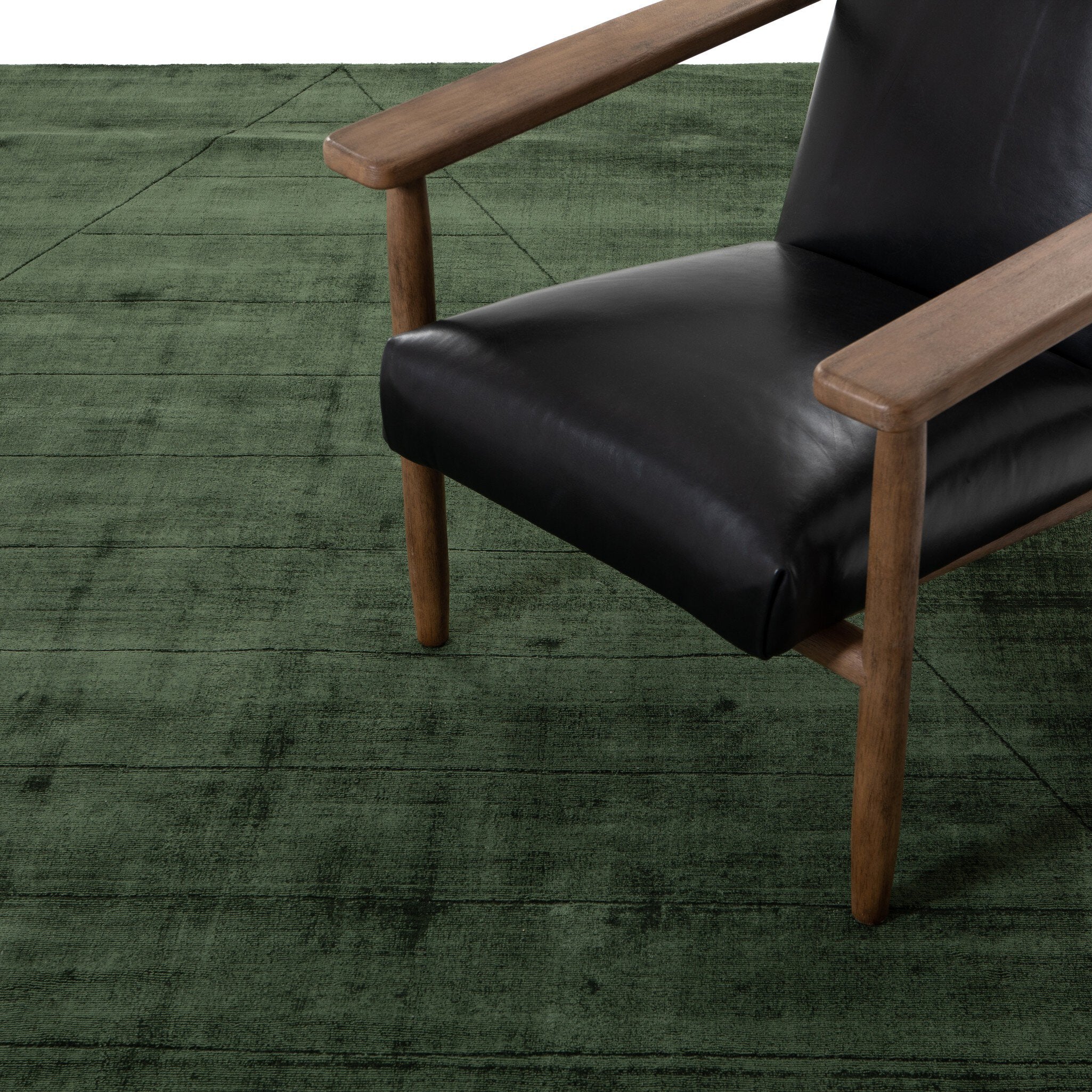 Black leather chair with wooden arms and legs on a green textured floor.