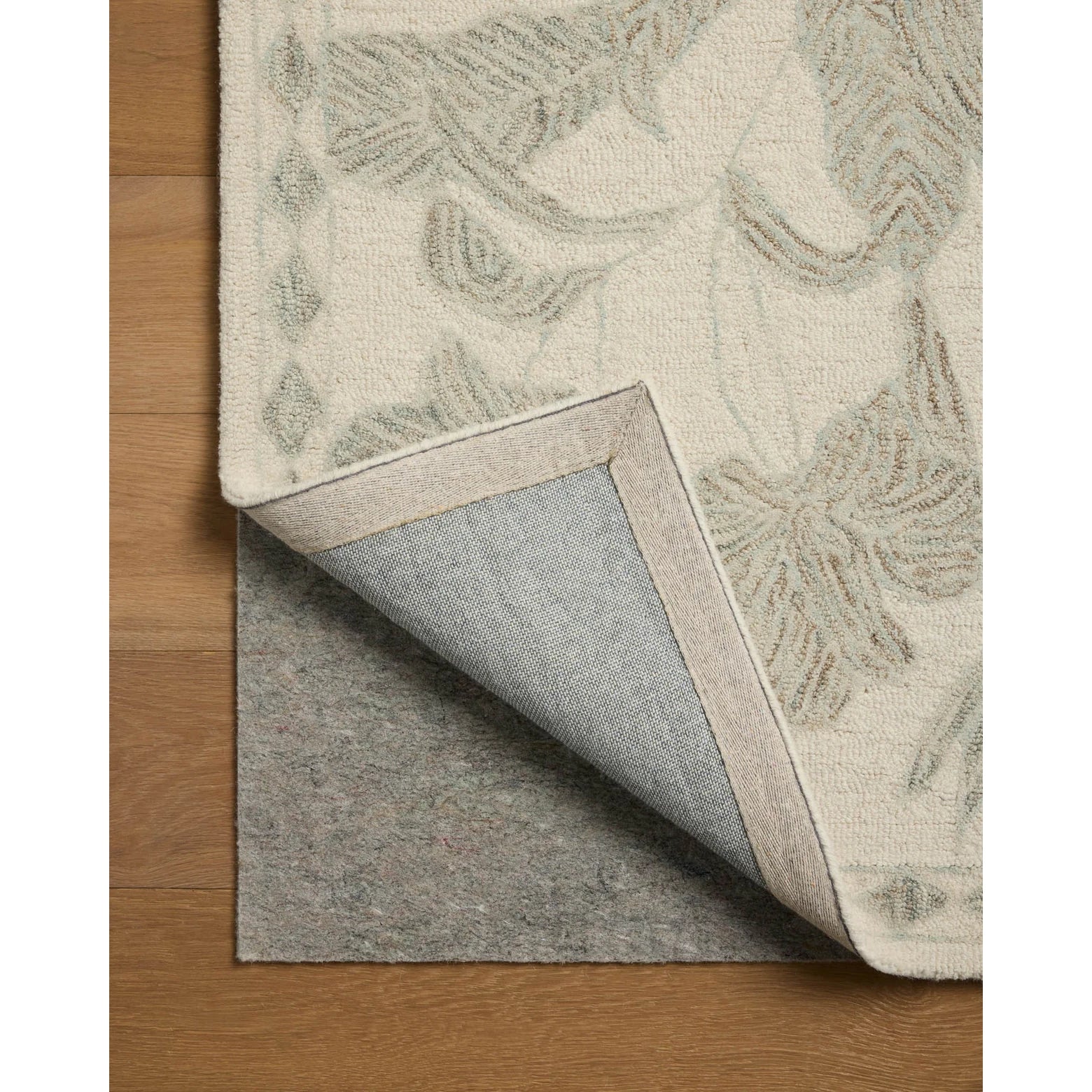 Close-up of a patterned beige rug with a gray underlay on a wooden floor.