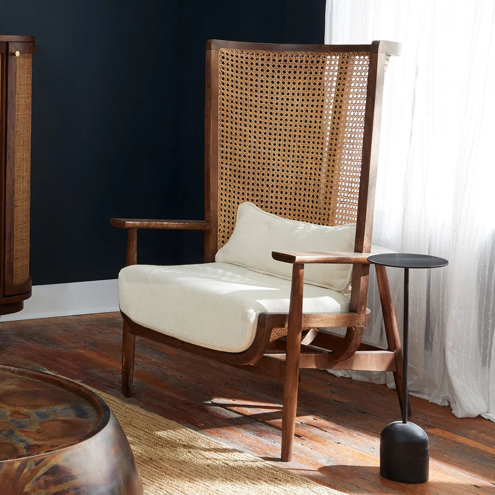 Wooden armchair with wicker backrest and white cushion in a room with dark walls and a window with white curtains.