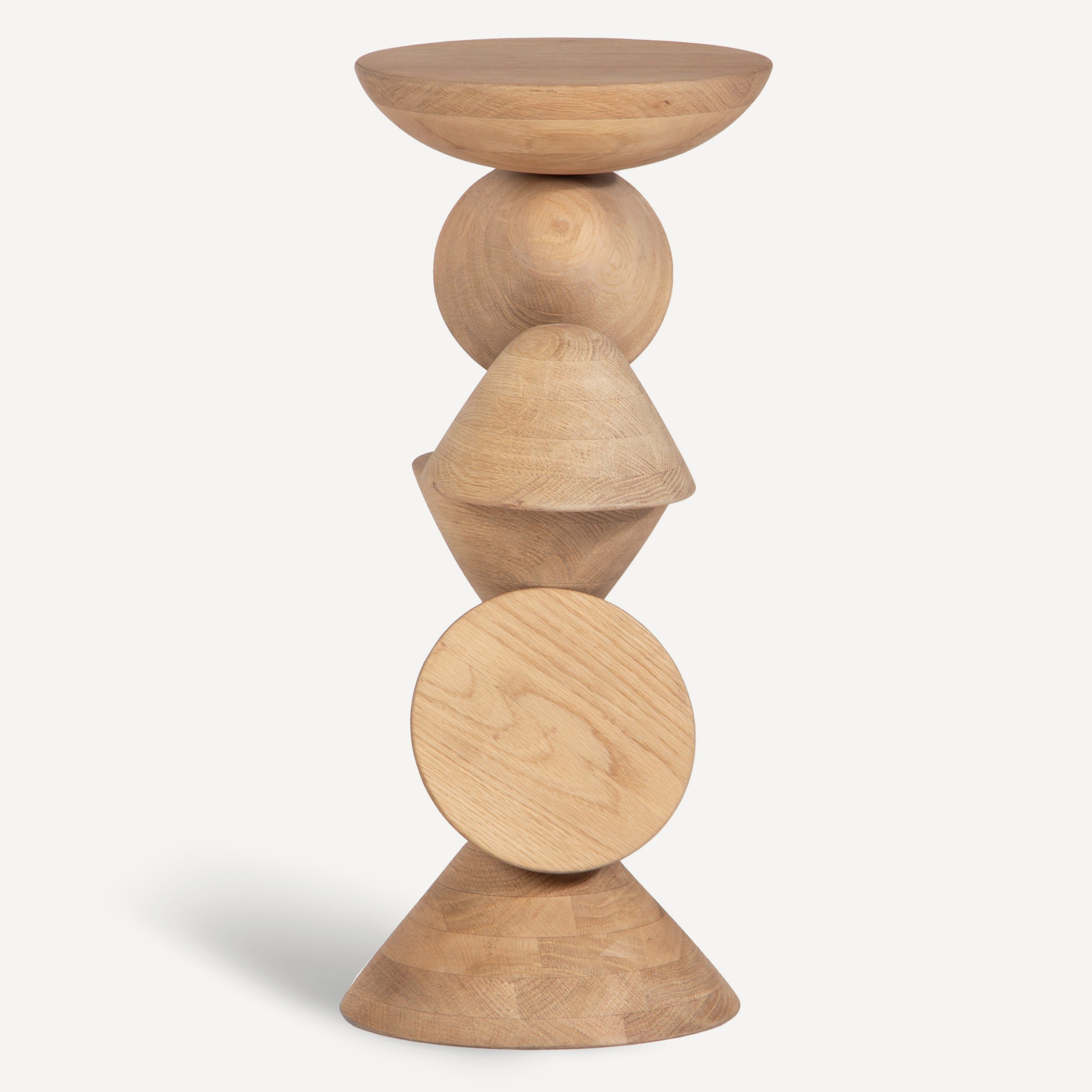 A modern wooden side table with a stacked geometric design, featuring a bowl, sphere, cone, oval, and pyramid shape in a light natural wood finish, set against a plain off-white background.