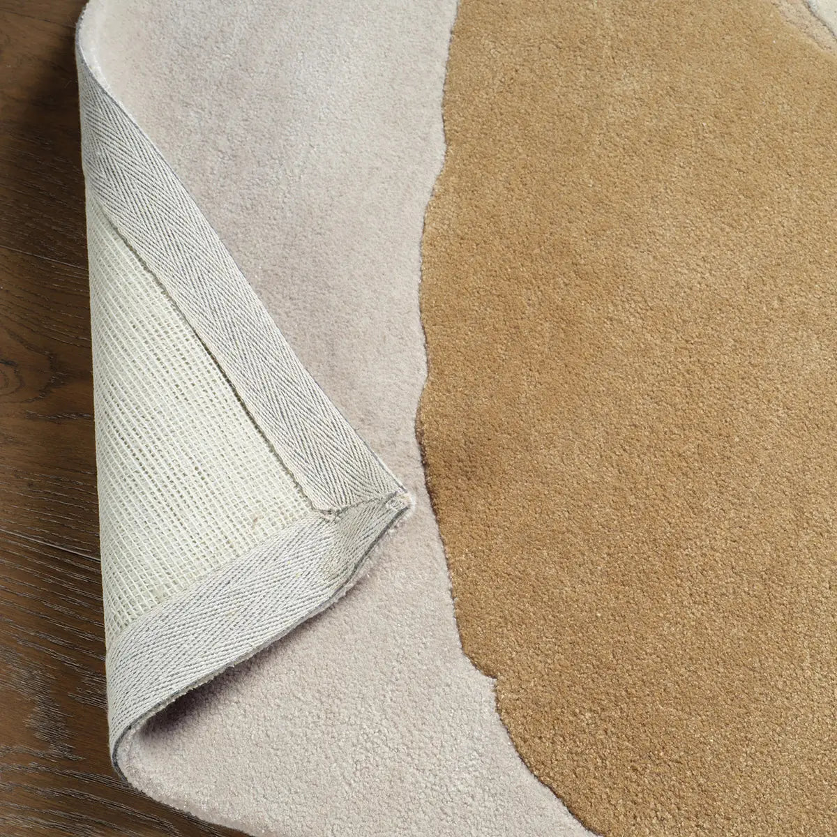 Close-up of a beige and brown rug corner on a wooden floor.