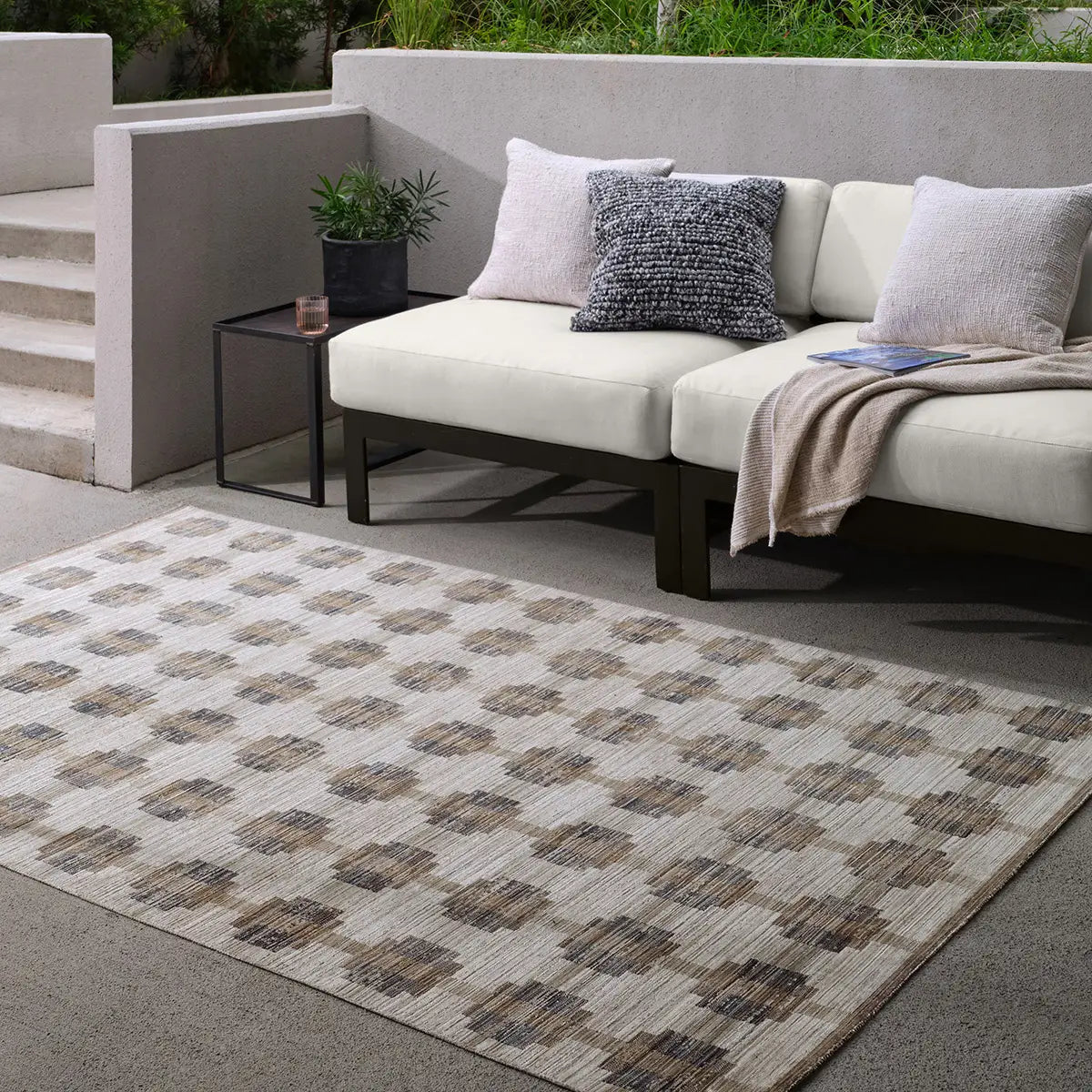 Outdoor seating area with a patterned rug, sofa, and small table.