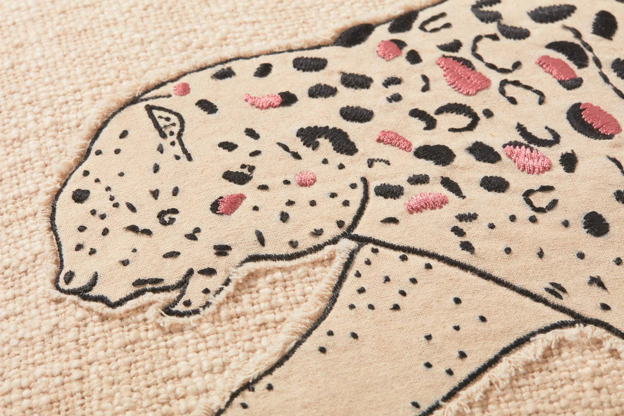Embroidered design of a snow leopard on a beige fabric background