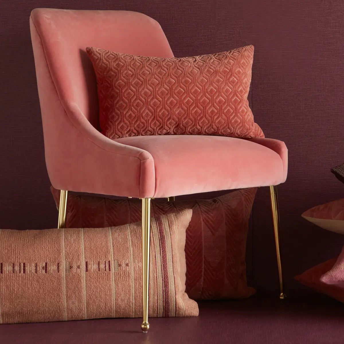 Pink velvet chair with gold legs against a maroon wall