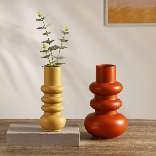 Two decorative vases, one yellow and one red, on a wooden surface with a neutral background.