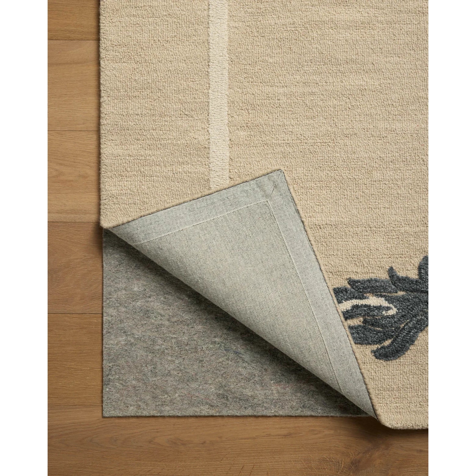 Close-up of a beige rug with a non-slip backing on a wooden floor.