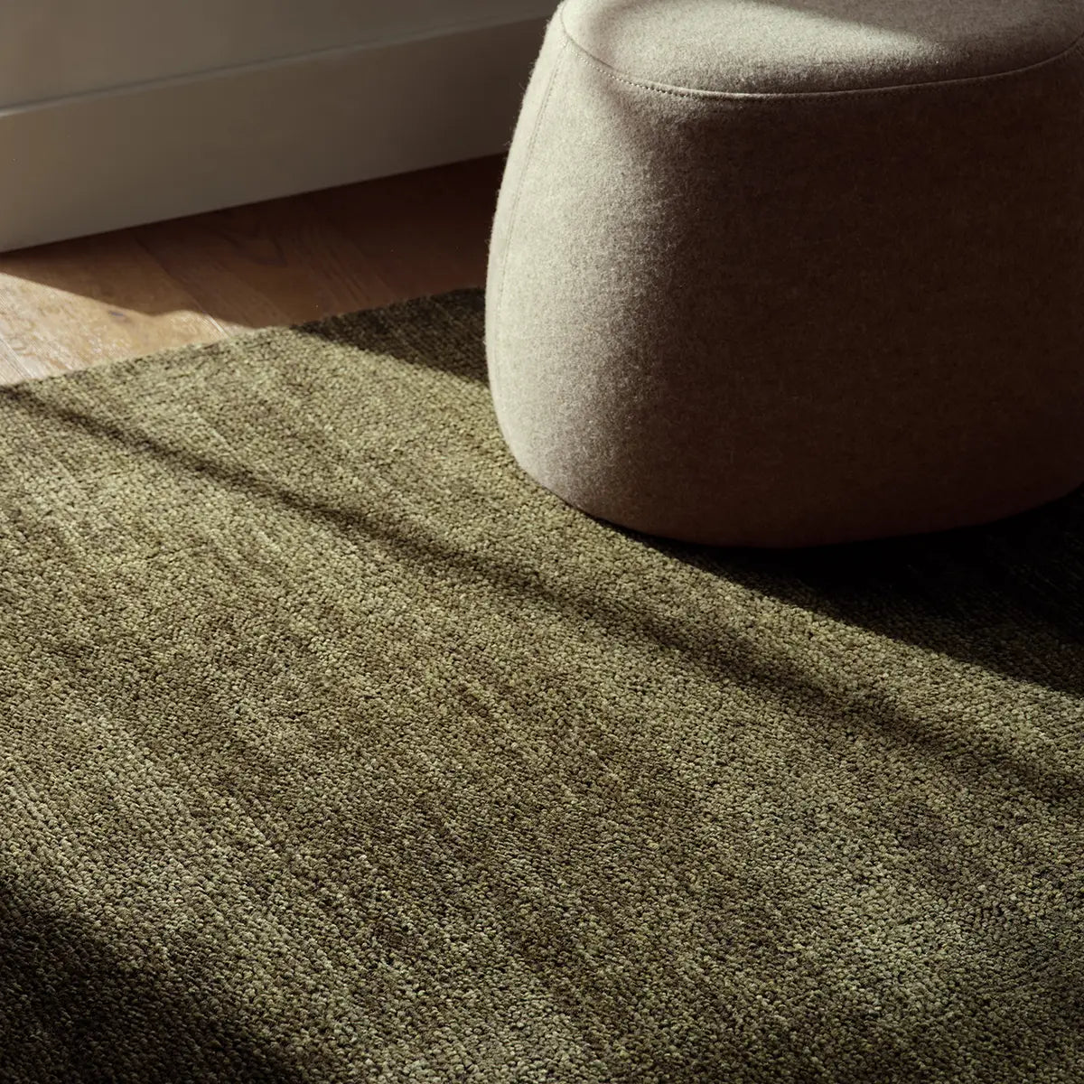Close-up of a textured green area rug with a beige ottoman in the corner.