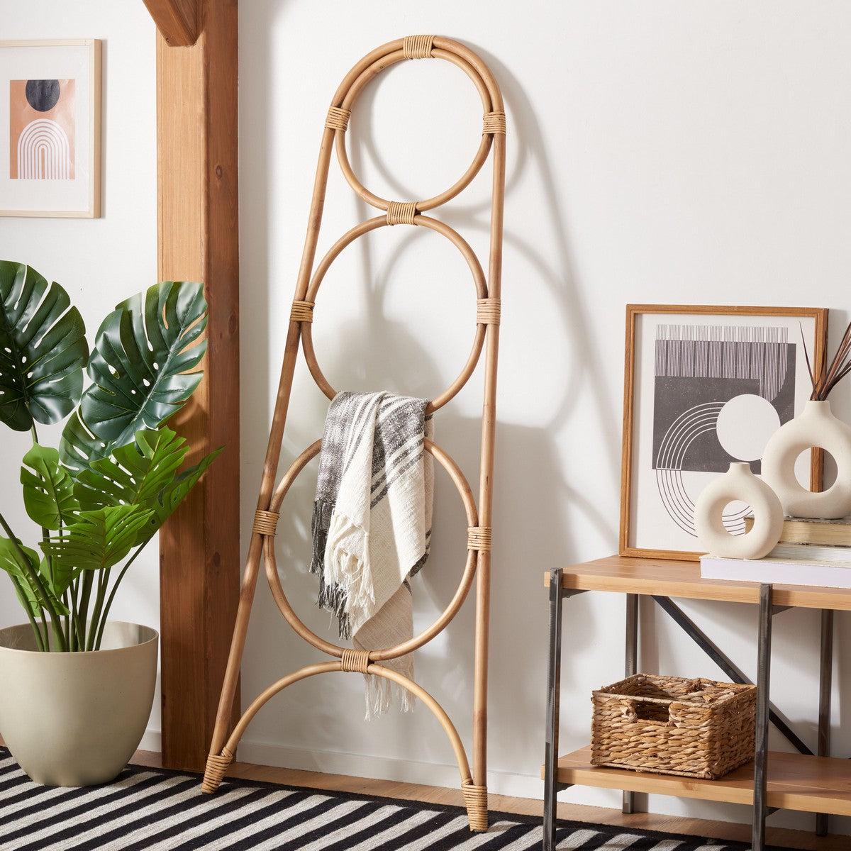 Rattan ladder with a towel against a white wall in a room with a plant and a small table.