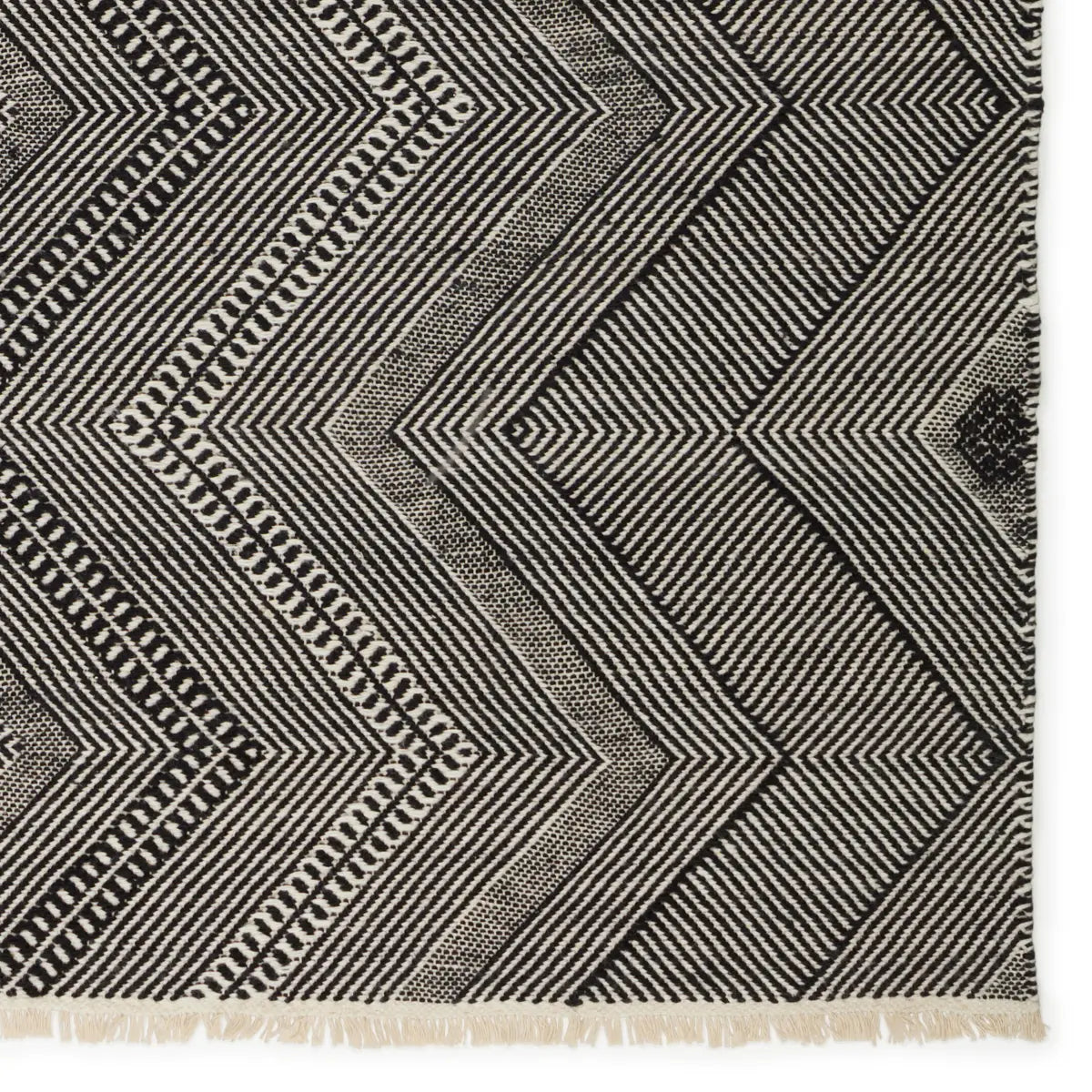 Black and white geometric patterned rug with fringes on a plain background