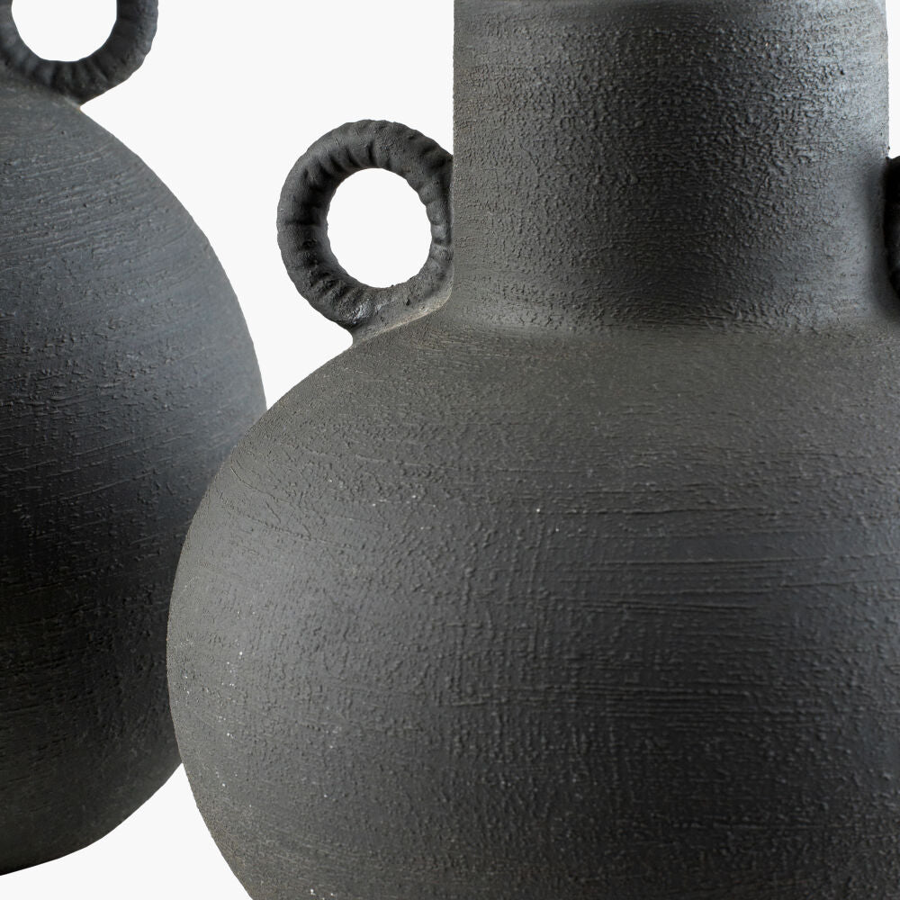 Close-up of a textured black ceramic vase with circular handles on a white background