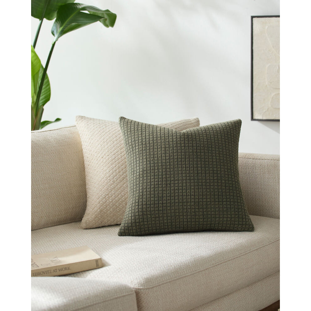 Green textured pillow on a beige sofa with a plant and framed picture in the background
