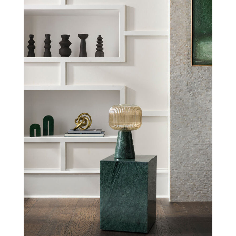 Decorative lamp on a marble pedestal in a room with shelves and art.
