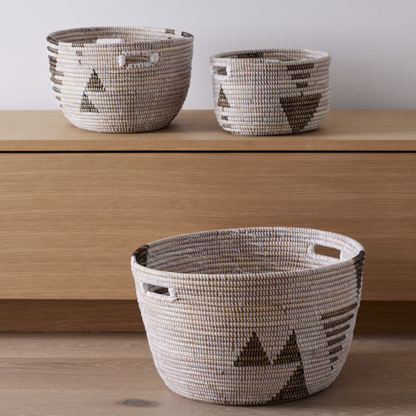 Three woven baskets with geometric patterns on a wooden surface.