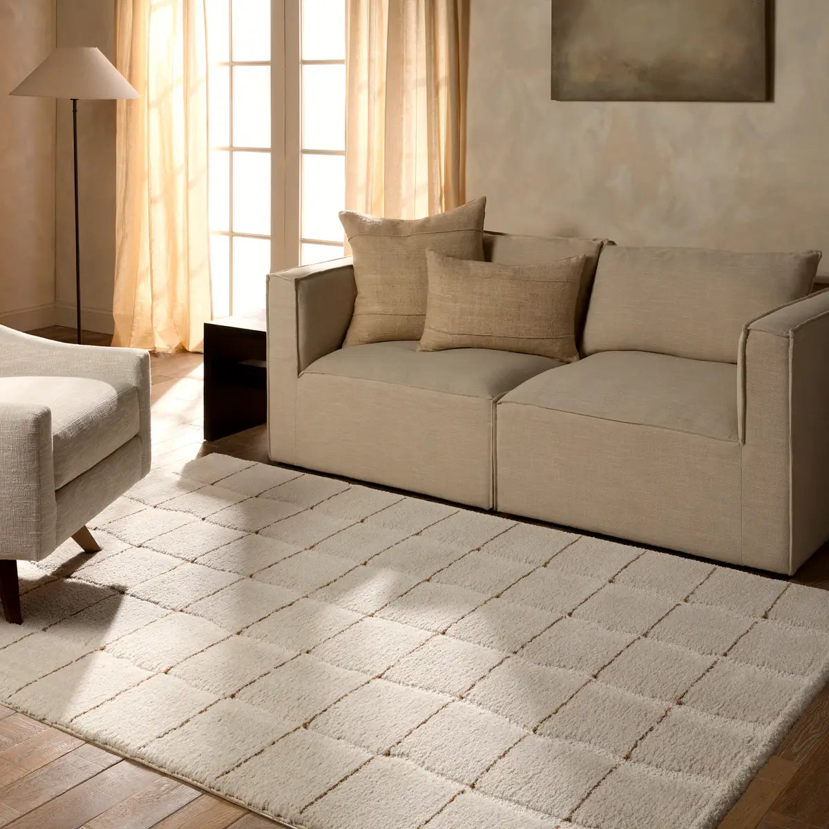 Beige sofa with cushions in a living room setting with a rug and lamp.