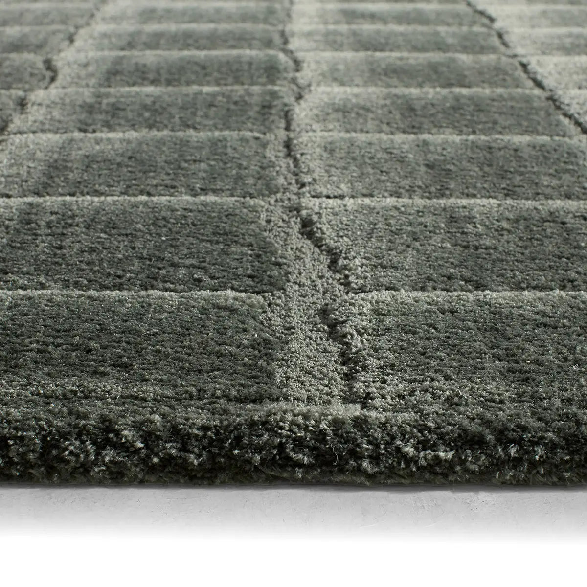 Close-up of a textured green rug with a geometric pattern on a light background