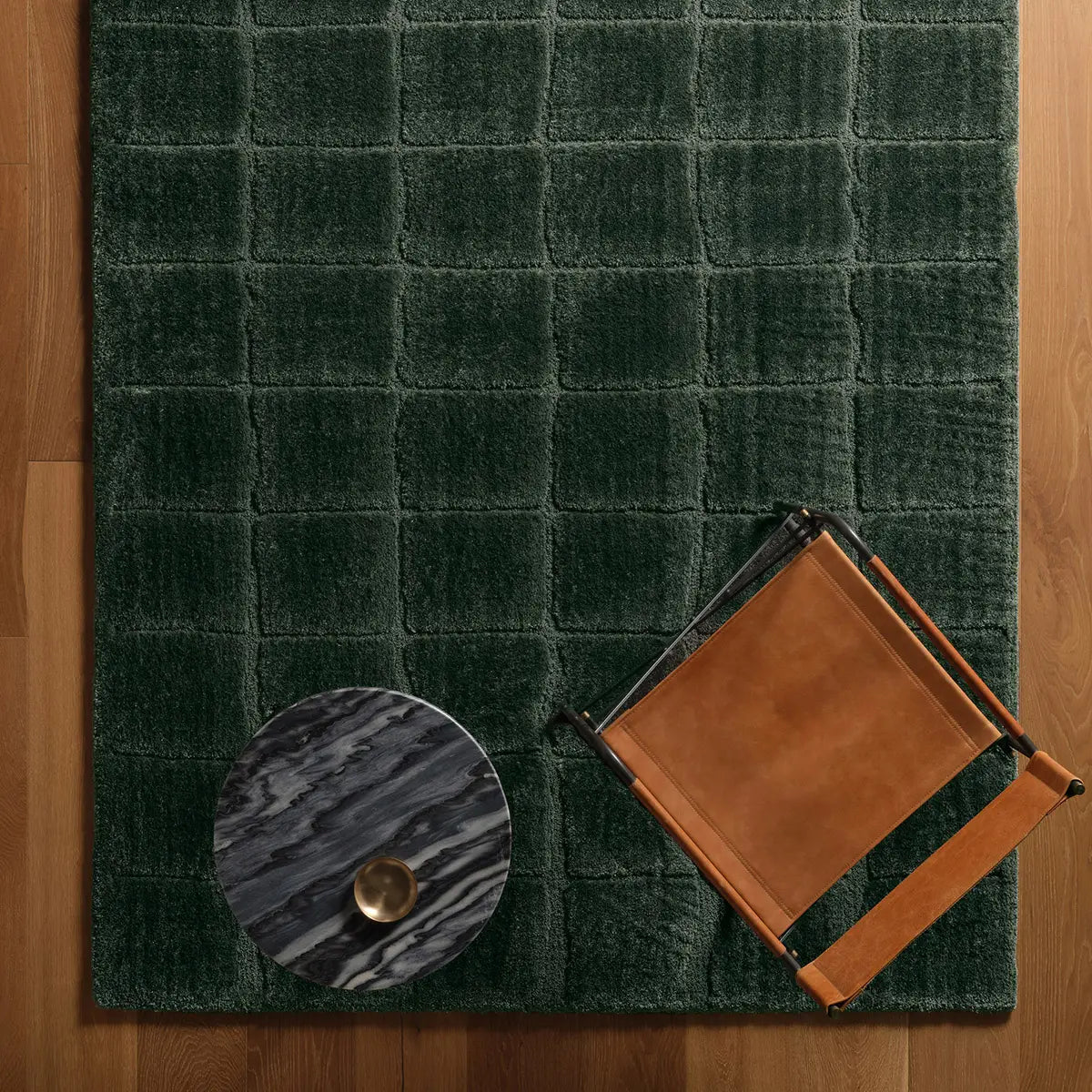 Green checkered rug with a brown leather bag and round decorative item on a wooden floor.