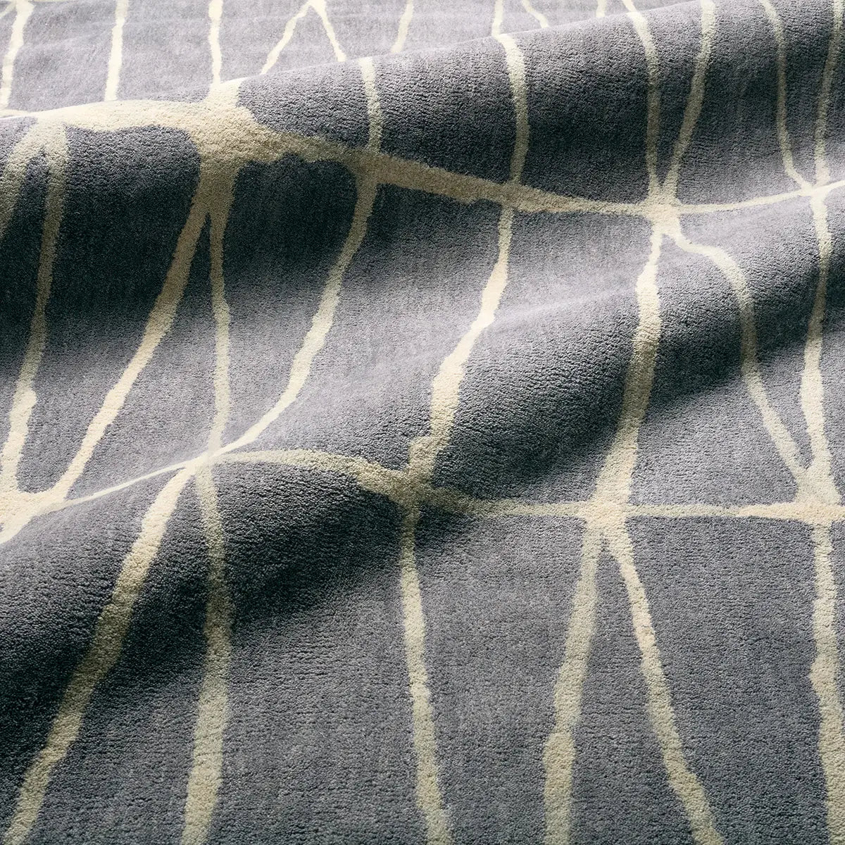 A close-up of a textured fabric with a geometric pattern of thick cream-colored lines on a slate gray background.
