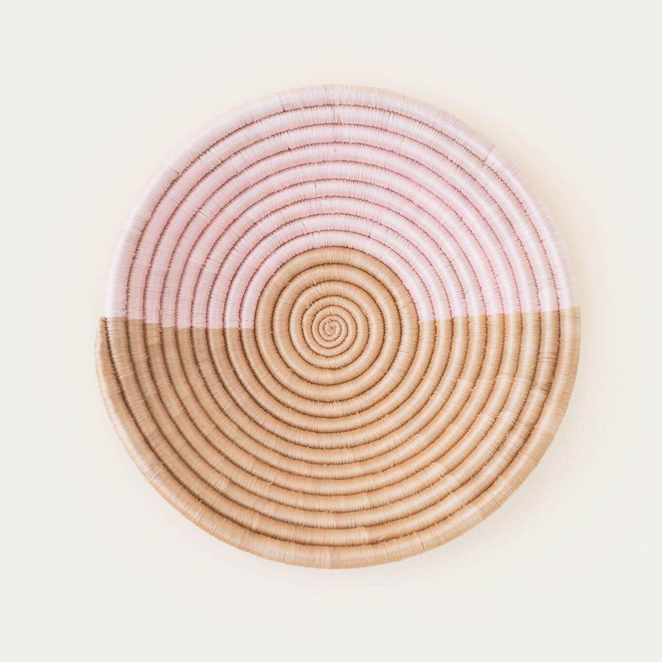 Round woven basket with pink and beige concentric circles on a white background