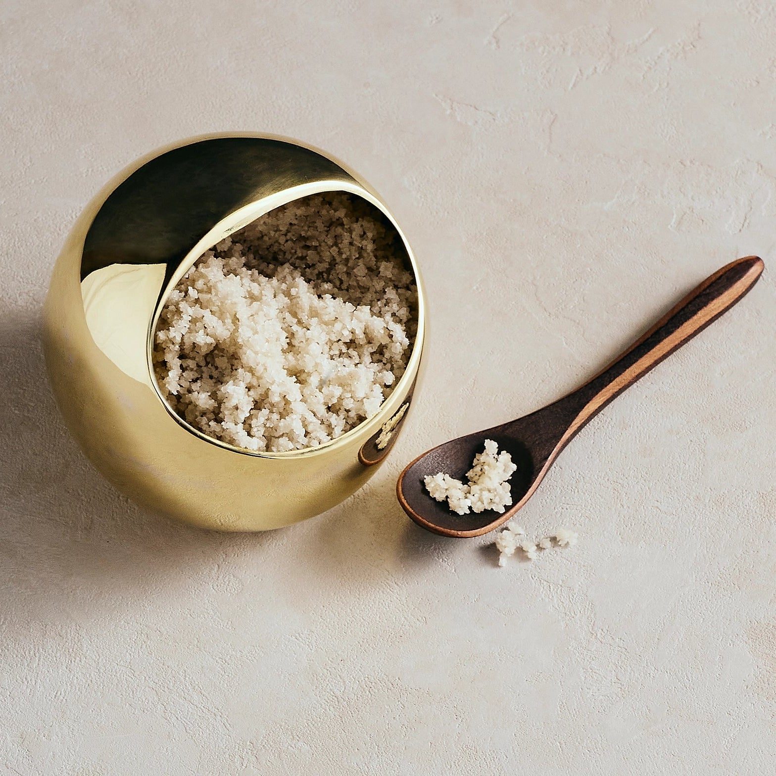 Gold salt cellar with a wooden spoon on a beige background