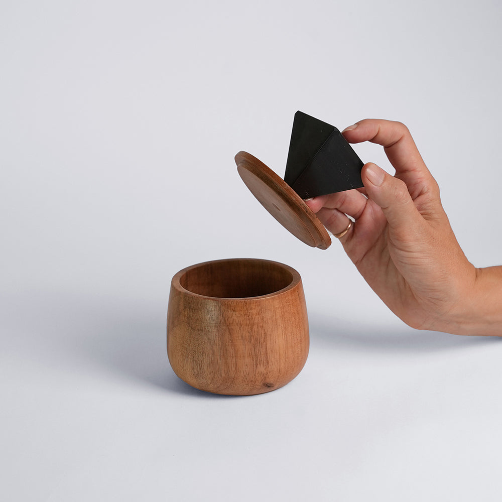 Wooden box with a hand holding a black triangle-shaped handle on a light gray background