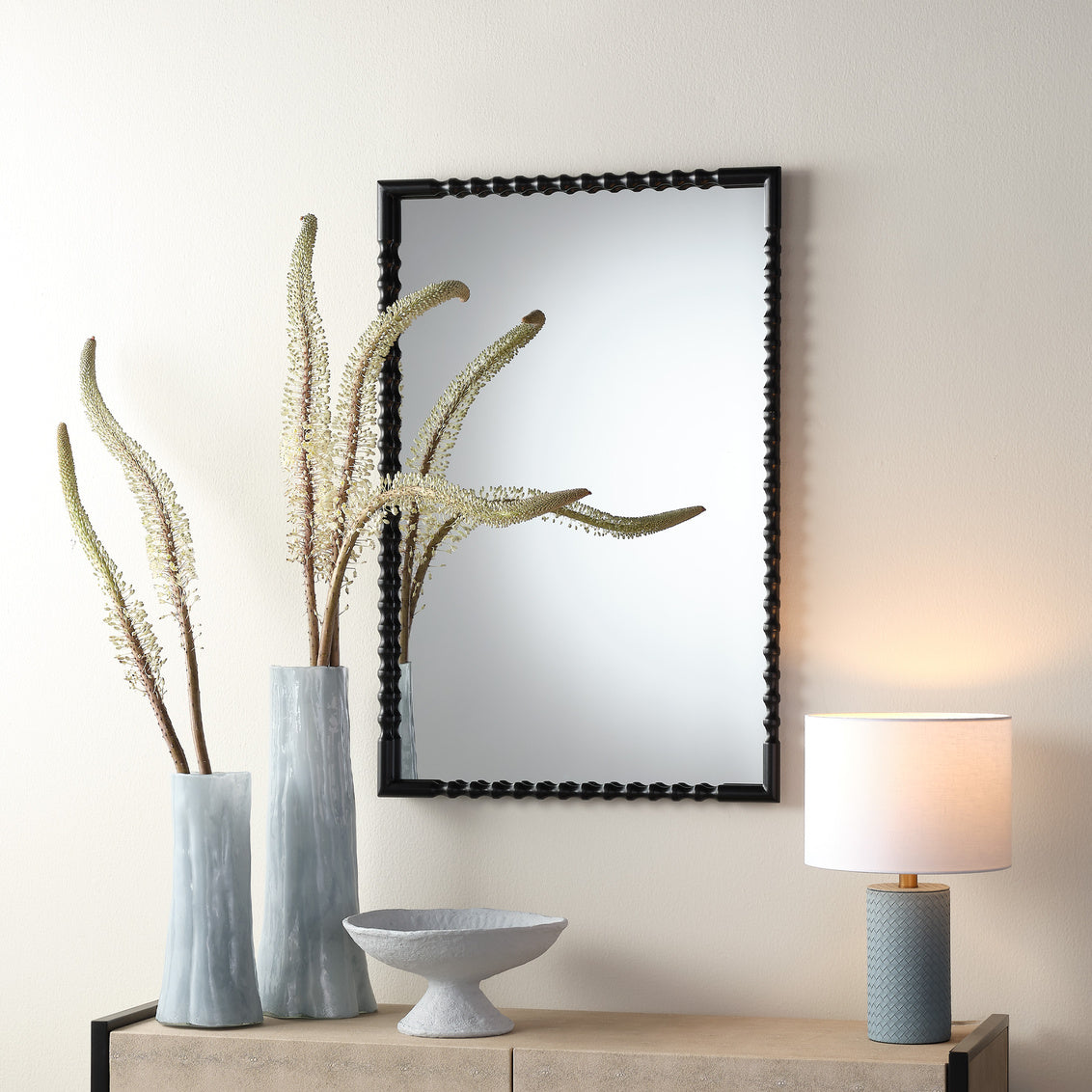 Decorative items including a mirror, vase with dried plants, bowl, and lamp on a wooden surface.
