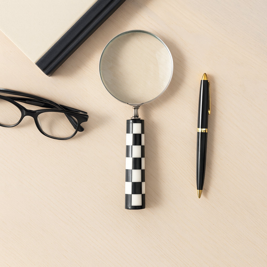 Magnifying glass, glasses, and pen on a beige surface