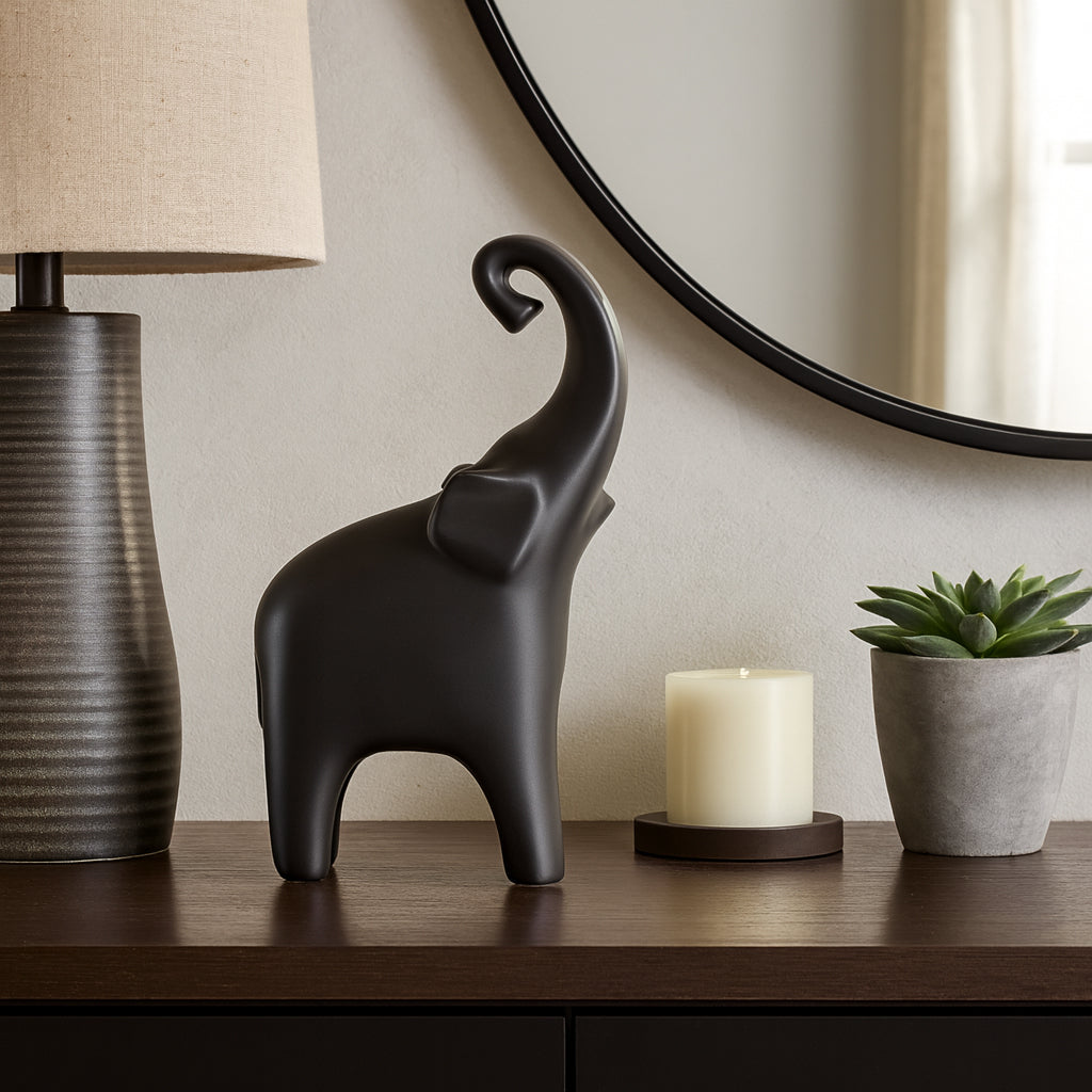 Decorative elephant figure on a table with a lamp, candle, and plant in the background.