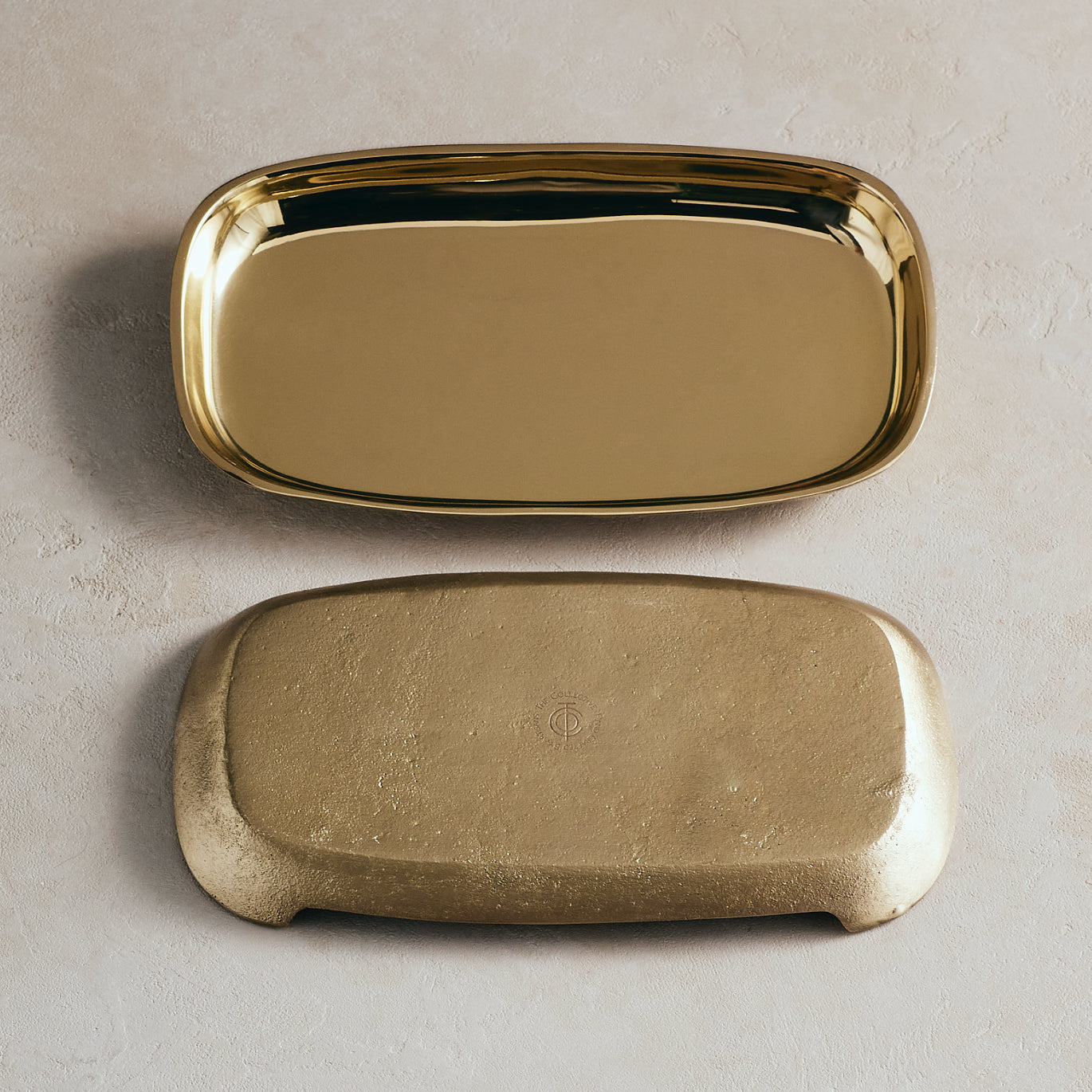 Two gold trays, one smooth and one textured, on a beige background