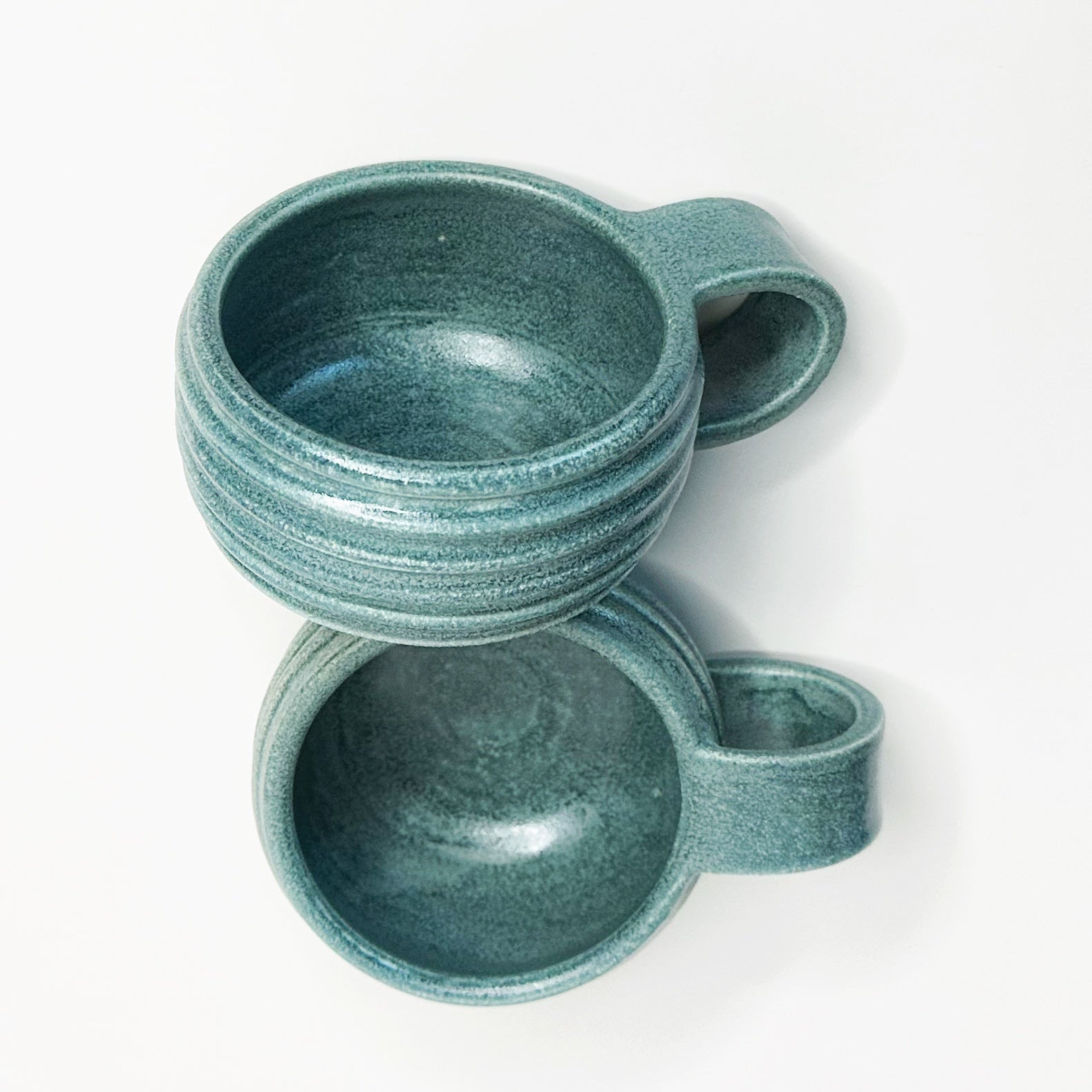 Two teal ceramic cups stacked on a white background