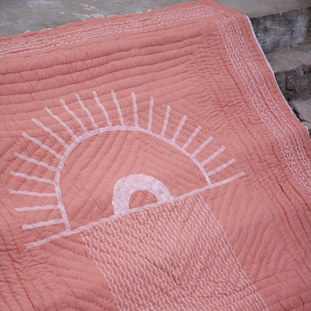Pink quilt with embroidered design on a stone surface