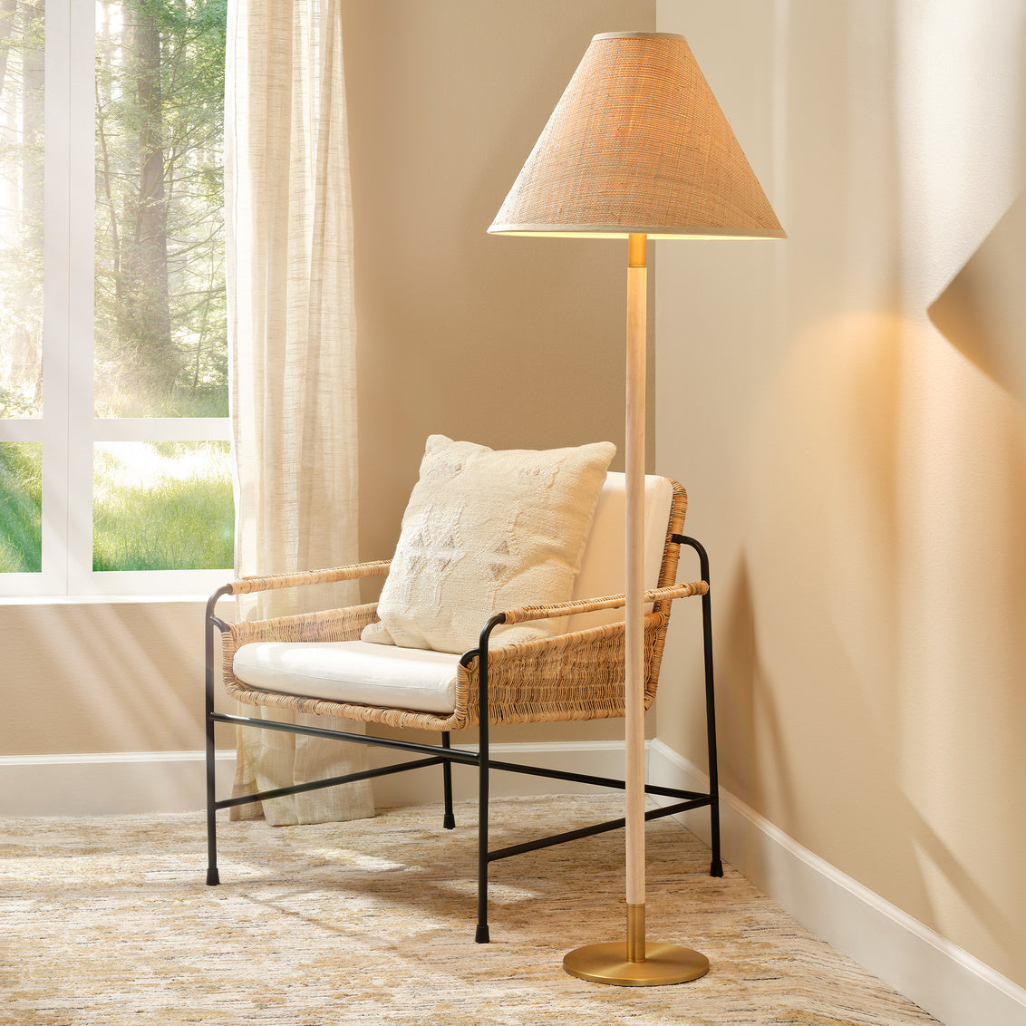 Wicker chair with white cushion next to a standing lamp in a room with a window and curtains.