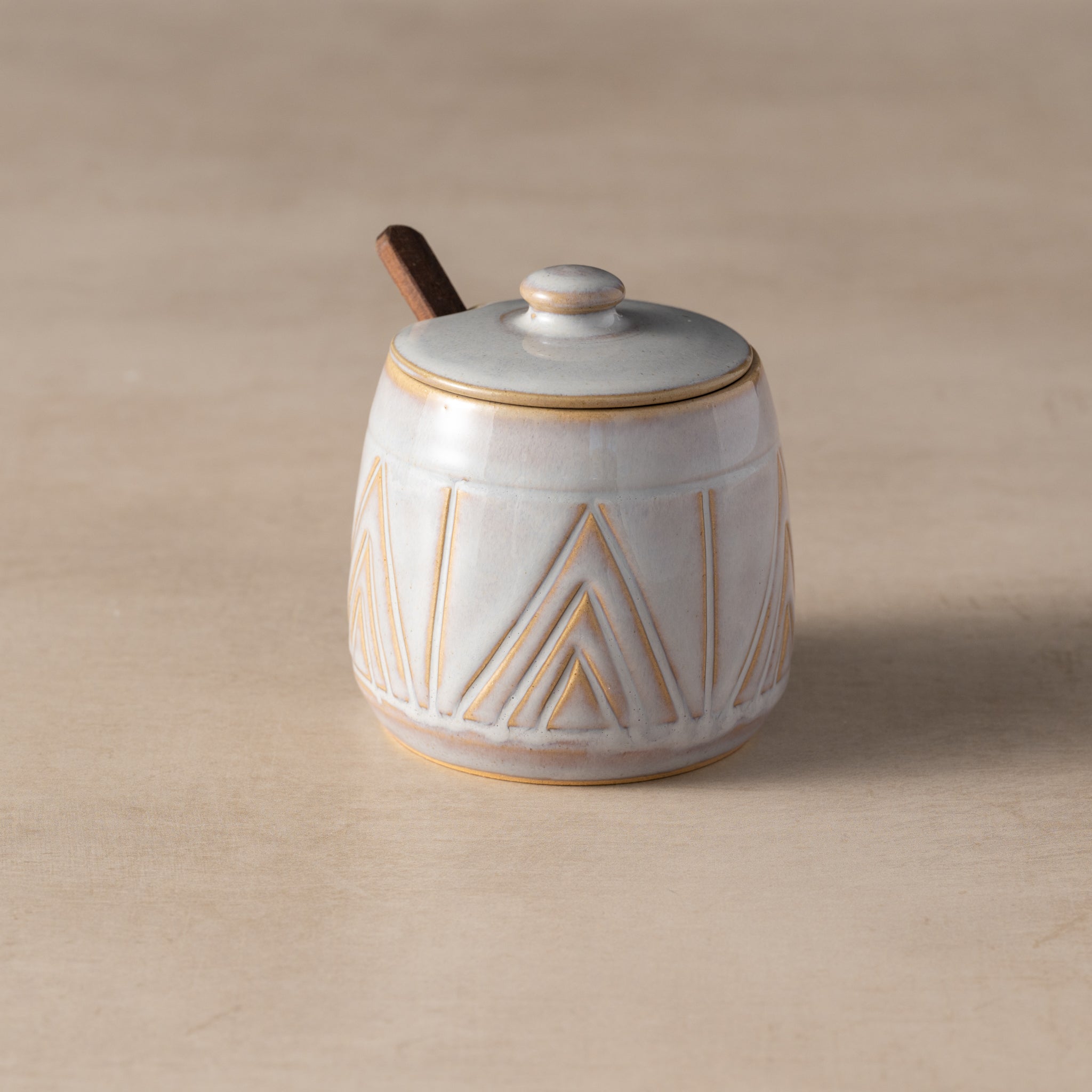 Ceramic jar with geometric design and wooden spoon on beige background