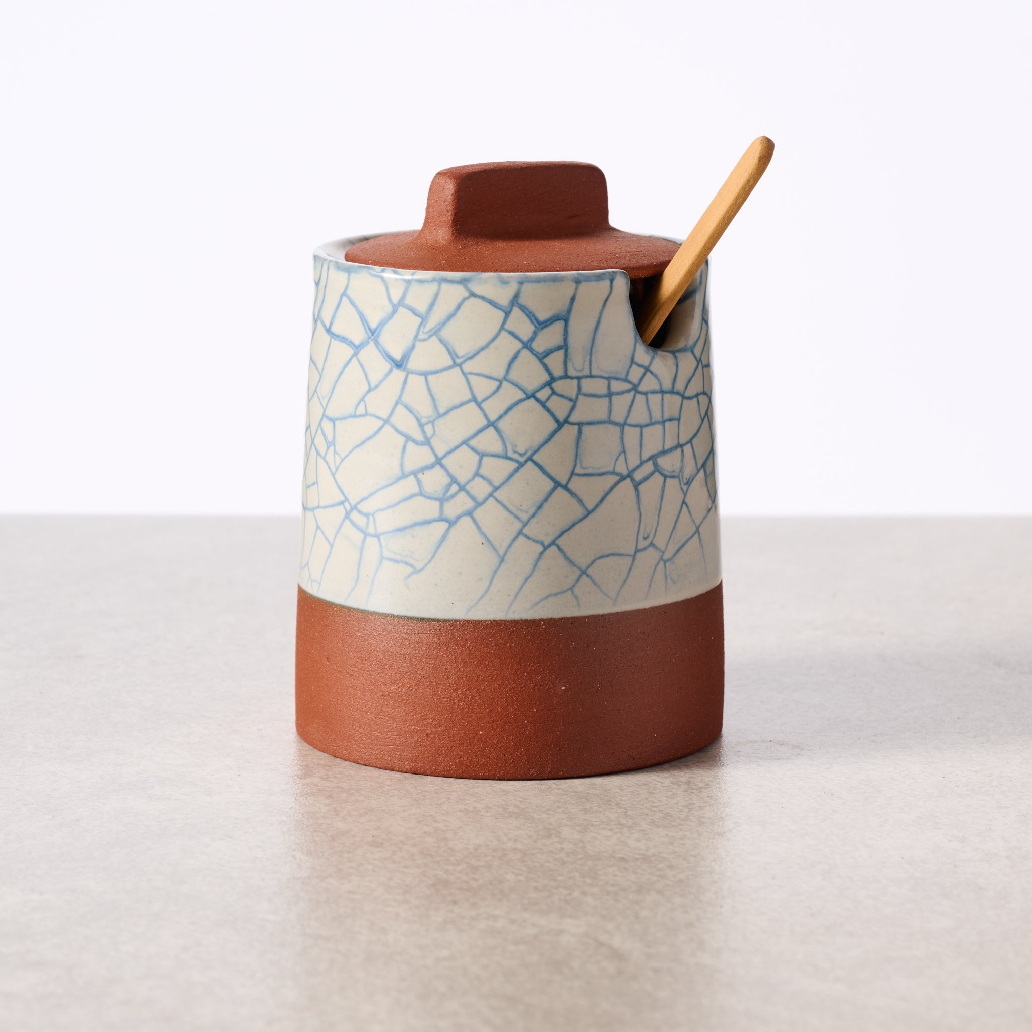 Ceramic container with textured surface and wooden spoon on a light background