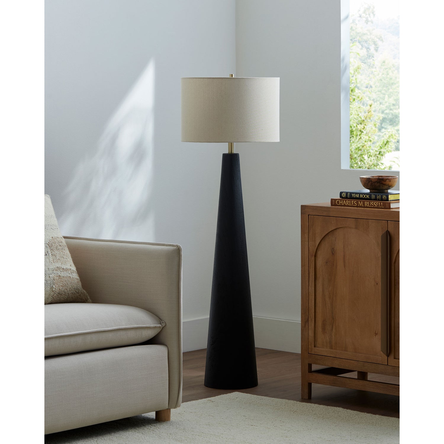 Floor lamp with a black base and beige shade in a living room setting.