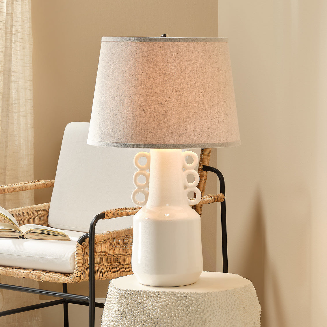 Beige ceramic lamp with decorative rings on an end table beside a coastal accent chair