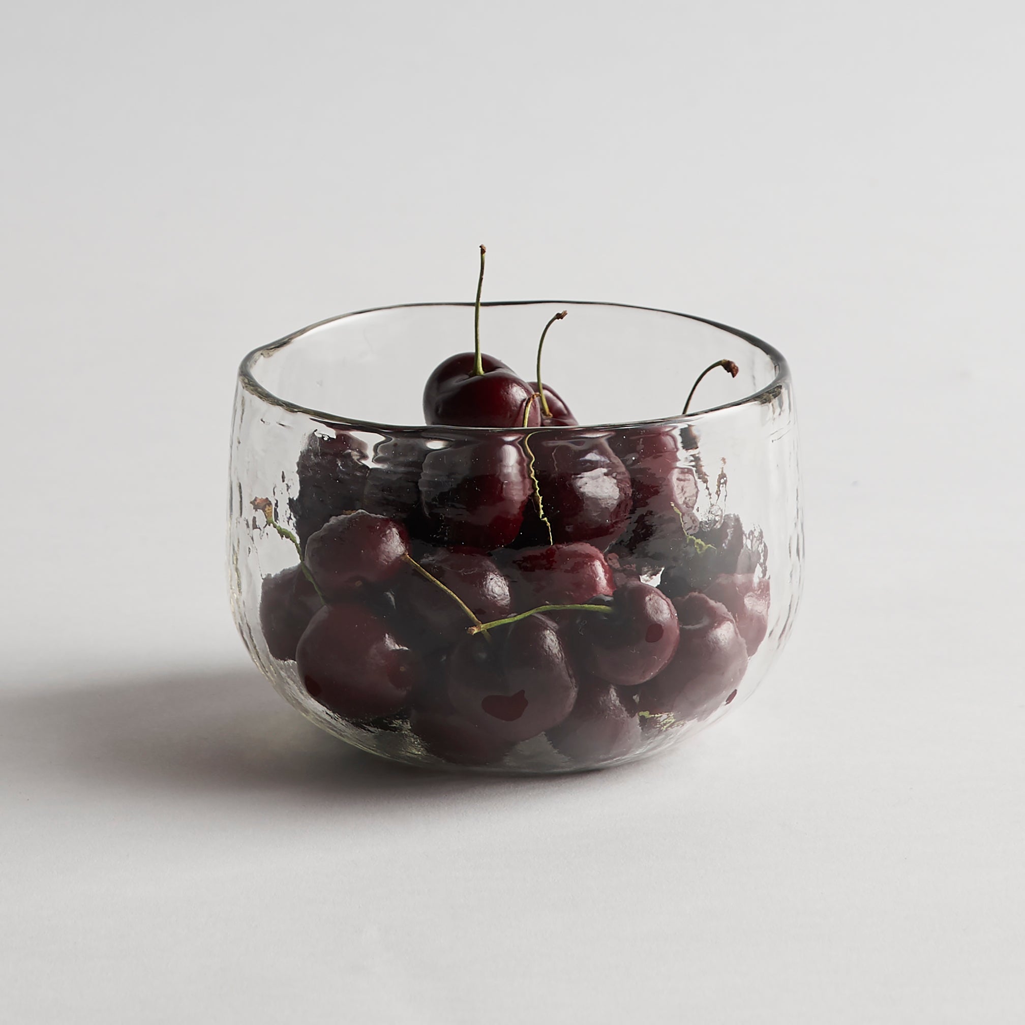 Clear glass bowl filled with cherries on a light gray background