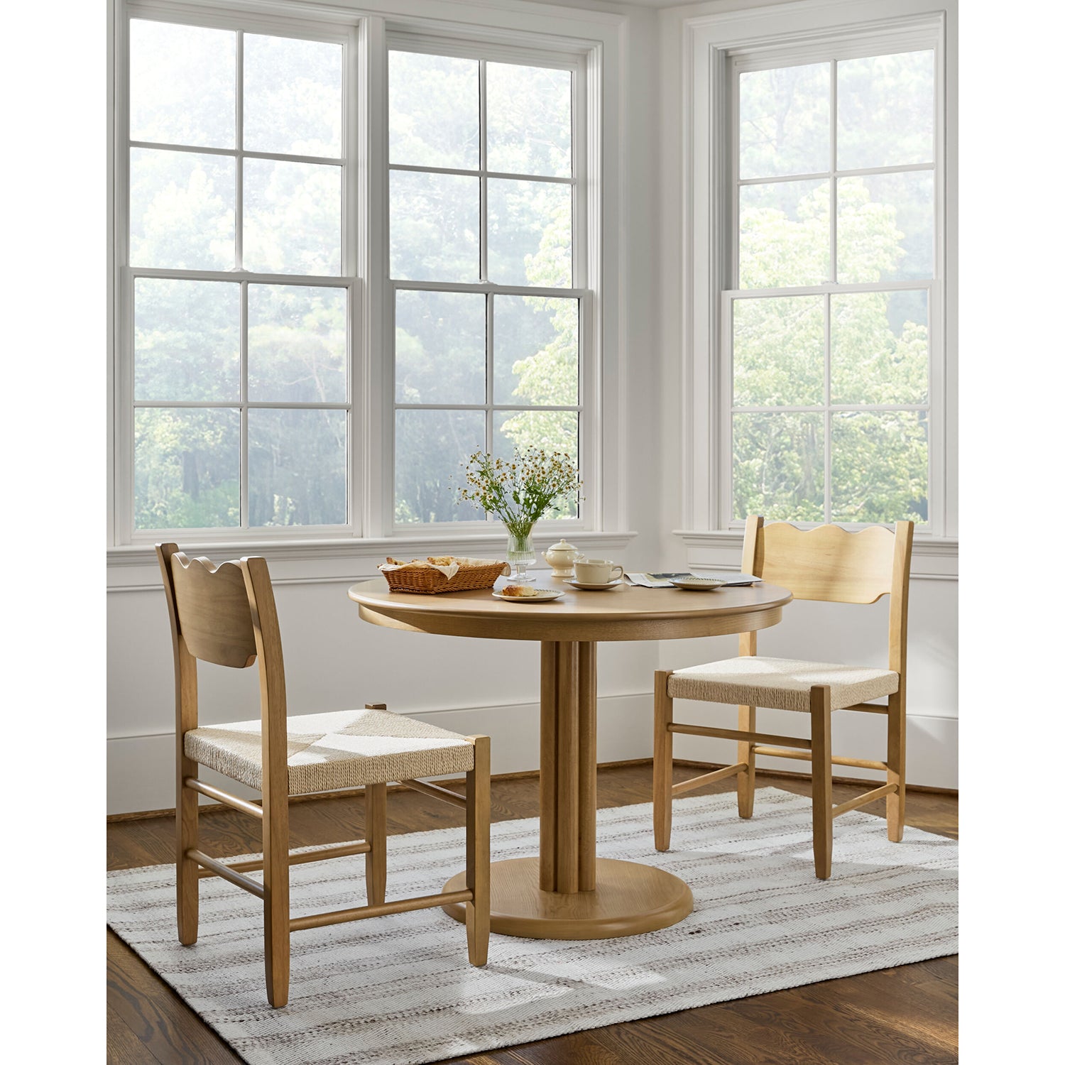 Dining room with wooden table and chairs in front of large windows.