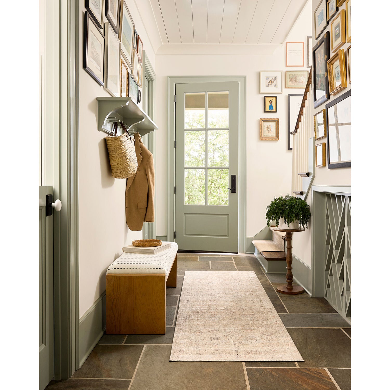 Entryway with coat rack, bench, and framed pictures on a white wall.
