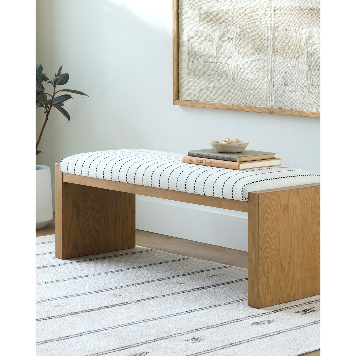 Wooden bench with a striped cushion in a room with a plant and framed artwork.